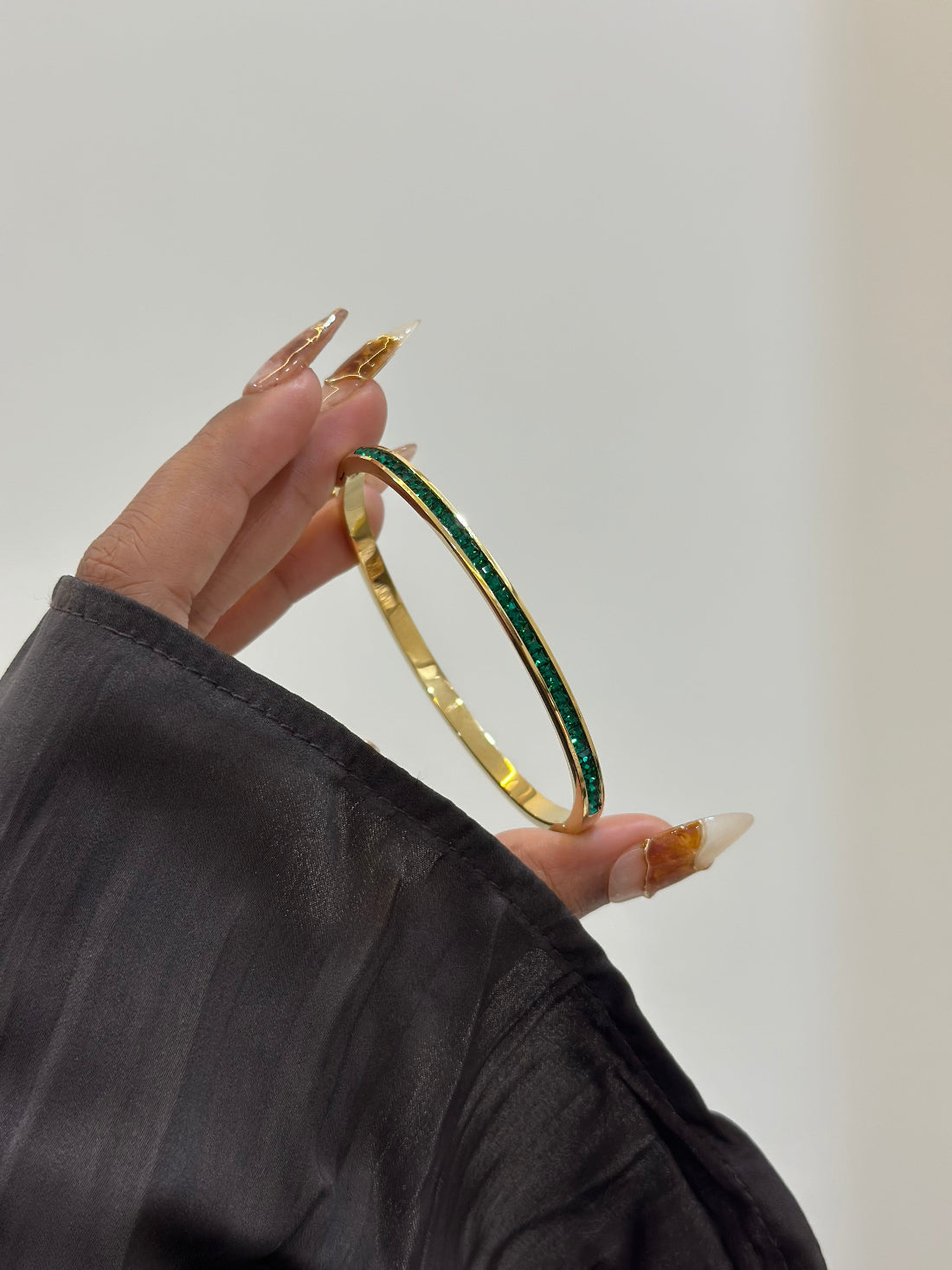 Gold bracelet with green stones held by a hand against a neutral background