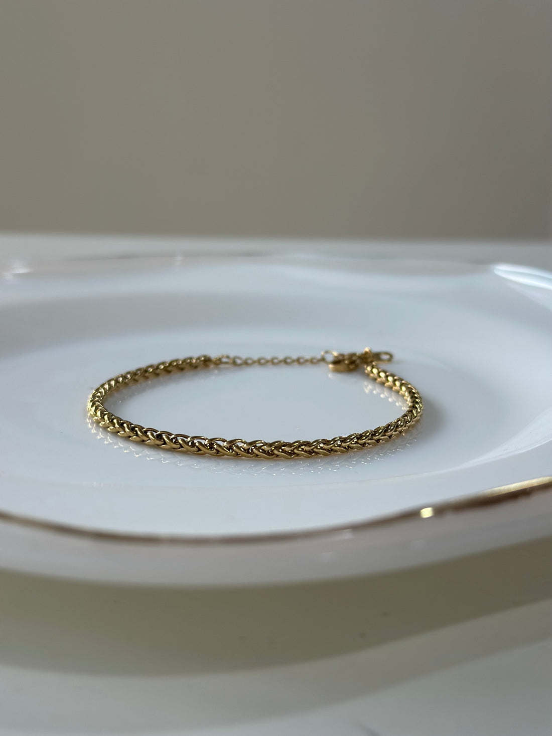 Gold bracelet on a white plate with a neutral background