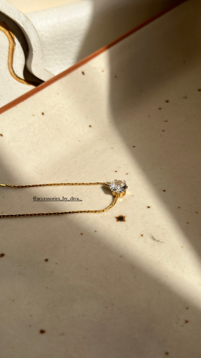 Gold necklace with a diamond pendant on a textured beige surface.