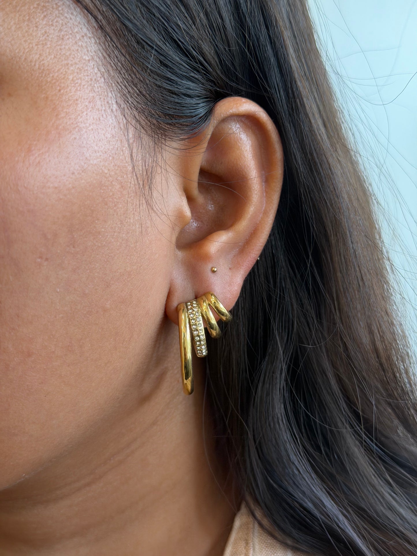 Close-up of an ear wearing a gold hoop earring with additional gold rings stacked on it.