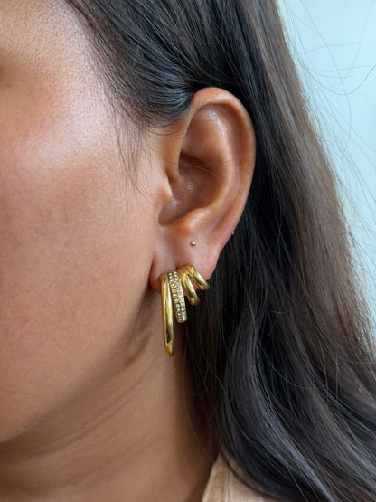 Close-up of an ear wearing a gold hoop earring with additional gold rings stacked on it.